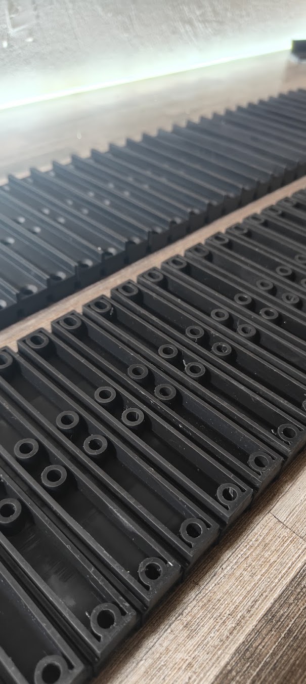 Rows of black printed machine covers and filler parts with ribs and circular mounting holes